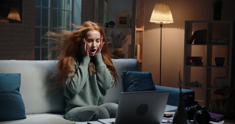 Pretty caucasian redhead girl looking at laptop screen, hair blowing, reading breaking news, seeing shocking discount during online shopping, vowing in amazement 4k footage
