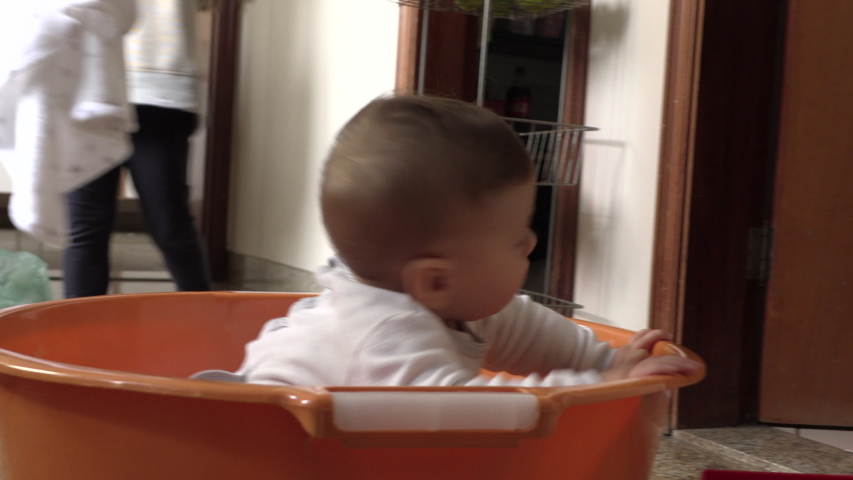 Adorable small baby toddler inside large plastic laundry bucket at kitchen