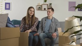 Smiling couple embracing on sofa and looking at cardboard boxes