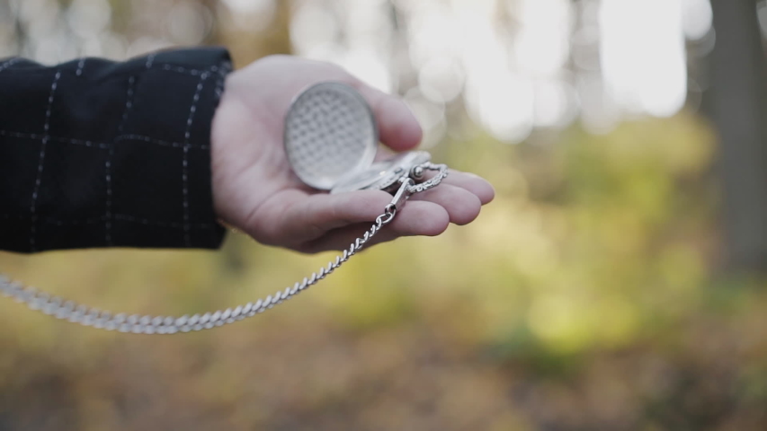 View of male hand holds watches pendant on blurred background. Slowly