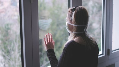 Woman at window with a mask in isolation for virus outbreak .