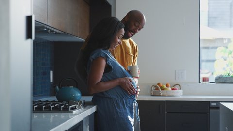 Loving african american husband with pregnant wife at home in kitchen feeling baby kick together - shot in slow motion
