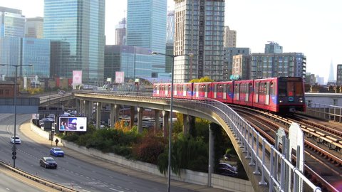 DLR train approaching East India station. The Docklands Light Railway, Car traffic at Aspen Way, Canary Wharf skyscrapers in the background. London, UK - November, 2018.