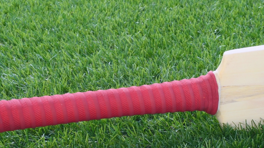 A low angle slider shot of a cricket bat and ball sitting in the grass
