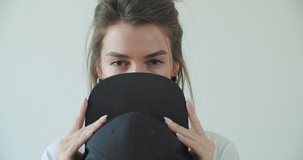 Hipster girl posing over withe wall. Street swag style, cap, beauty model face. Young woman cover her face black hat. 4k raw footage slow motion