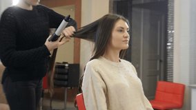Hairstylist using hair tongs and comb for hairstyling in beauty salon. Close-up hairdresser making wavy hair with tongs in hairdressing salon. 4k video