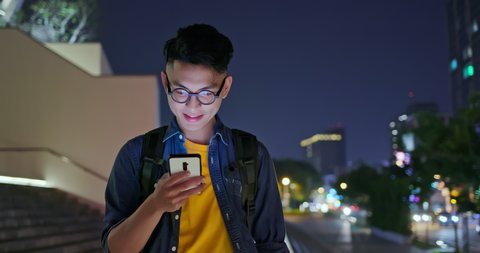 asian young man use smart phone outdoor and watch something interesting on it at night