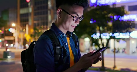 asian young man use smart phone while walking outdoor at night