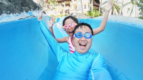 slow motion of asian girl with her dad enjoys water slide ride and take selfie in aquapark