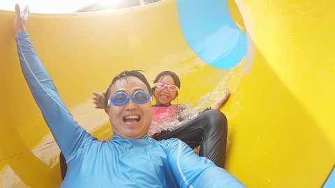 slow motion of asian girl with her dad enjoy water slide ride and take selfie in aquapark