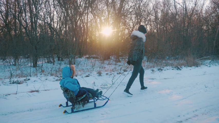Mom is carrying a child on a sled over the snow-covered forest. Cheerful winter vacation concept.