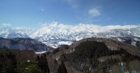 Hakuba Valley push in shot from drone showing the main ski resorts mid winter with lots of snow on a blue sky day.