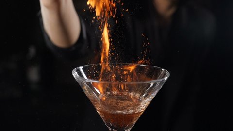 Bartender sets fire to cocktail, burning cinnamon in alcohol drink on black background. Flames in cocktail glass in slow motion, burning cinnamon in alcohol drink, barman makes drink. Full hd footage