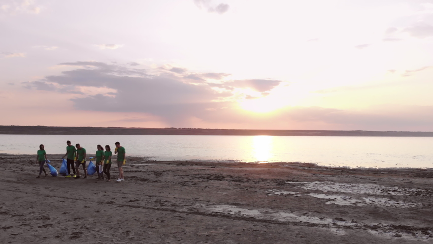 An optimistic group of volunteers takes out the trash from the beach against the backdrop of a beautiful sunset. Royalty-Free Stock Footage #1047199807