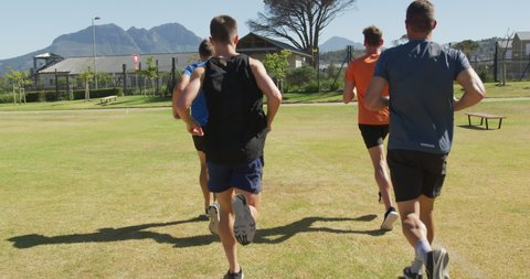 Rear view of a multi-ethnic group of male runners training at a sports field, running together on a grass track. Track and Field Sports Training in Stadium, in slow motion