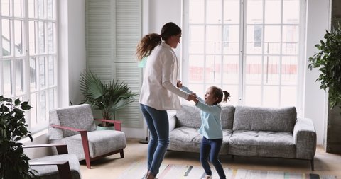 Happy young adult parent mum and small child daughter jumping having fun in living room, active cheerful baby sitter mother dancing with cute kid girl at home enjoy leisure activity together at home