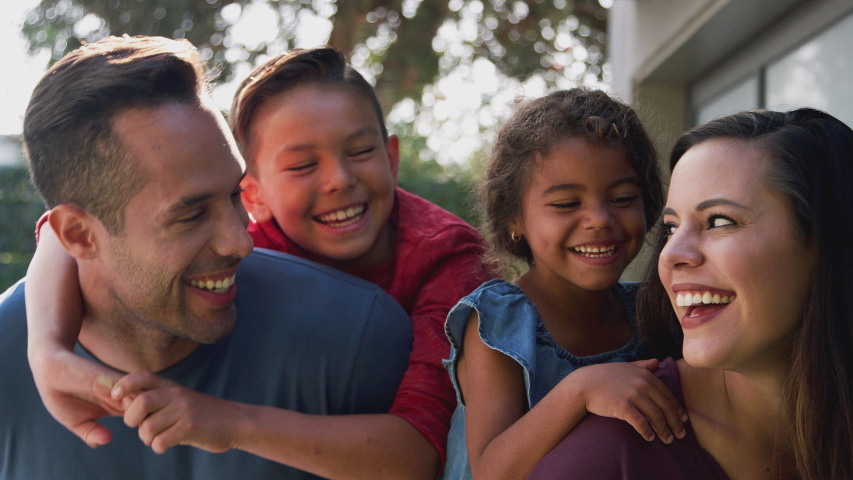 Portrait of smiling young hispanic family with parents giving children piggyback rides in garden at home against flaring sun - shot in slow motion Royalty-Free Stock Footage #1047202507