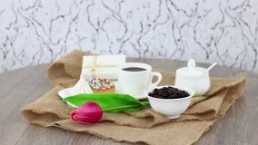 Cookies with coffee beans and cup with tulip on brown canvas on spinning wooden table background. FHD.