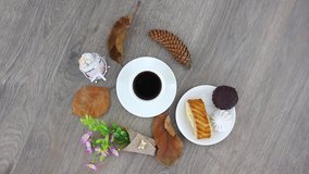 Top view spinning video of coffee cup with pastry sweets and dried leaves with cones. FHD.