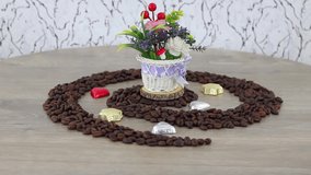 Coffee beans with candies and flowers pot on spinning wooden table background. FHD.