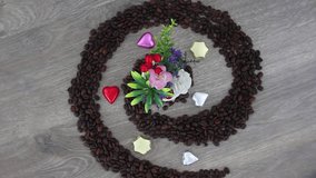 Top view spinning video of spiral coffee beans and candies with flowers in center. FHD.