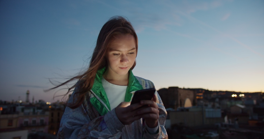 Portrait of nice pleasant Caucasian female staying up to date in social app outdoor, evening windy moment at terrace of happy cute girl influencer using smartphone online in internet connected Royalty-Free Stock Footage #1047205528