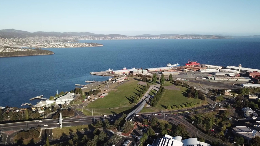 Slow aerial pan around cars driving into medium city during sunny evening, Hobart, Tasmania.