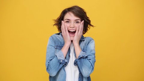 Fun beautiful brunette young woman in denim jacket white t-shirt posing isolated on yellow background in studio. People sincere emotions, lifestyle concept. Looking at camera found out heard good news