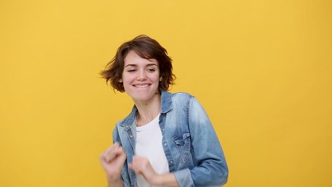 Fancy vivid cute brunette young woman in denim jacket white t-shirt posing isolated on yellow background in studio. People lifestyle concept. Dancing fooling around having fun gesticulating with hands