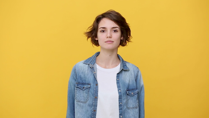 Smiling overjoyed beautiful brunette young woman in denim jacket white t-shirt posing doing winner gesture, say Yes isolated on yellow background in studio. People sincere emotions, lifestyle concept Royalty-Free Stock Footage #1047209302