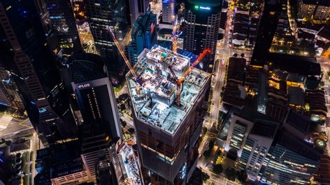 Singapore, Singapore - Feb 8, 2020: Time-lapse of under construction site, crane, car traffic transportation at night in Singapore city downtown. Drone aerial top view. Industrial business concept