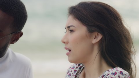 Handsome young black man and beautiful caucasian woman laying on the beach, talking, looking at the horizon. Medium shot on 4K RED camera with shallow depth of field.