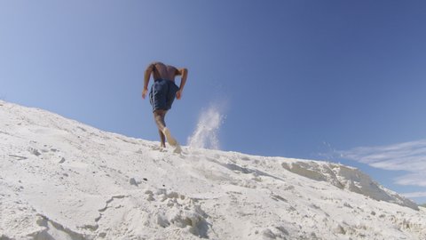 Sexy black milliennial man runs up sand dune on beach under blue sky in Australia. Medium to long shot on 4K RED camera.