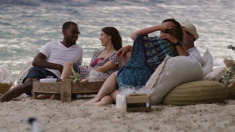 Sexy brunette joins her boyfriend and millennial friends at a picnic on sandy beach in Australia. Long medium shot on 4K RED camera.