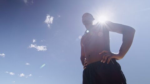 Fit shirtless black man on beach under sunny blue sky in Australia. Medium to closeup on 4K RED camera.