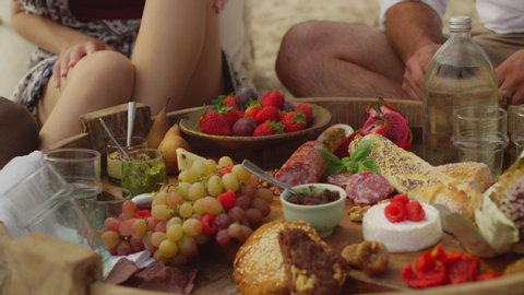 Friends enjoying a picnic of fruit, spreads, meat, cheese and bread on the beach in Australia with soft day lighting. Close up shot on 4k RED camera