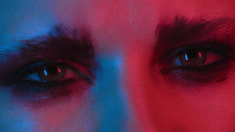 Girl opens her eyes, close-up portrait. Eyes and lips of young woman in neon light. Fashion bold makeup