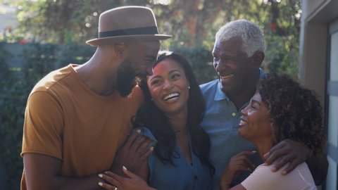 Portrait of senior African American parent talking and laughing with adult son and daughter in garden at home - shot in slow motion
