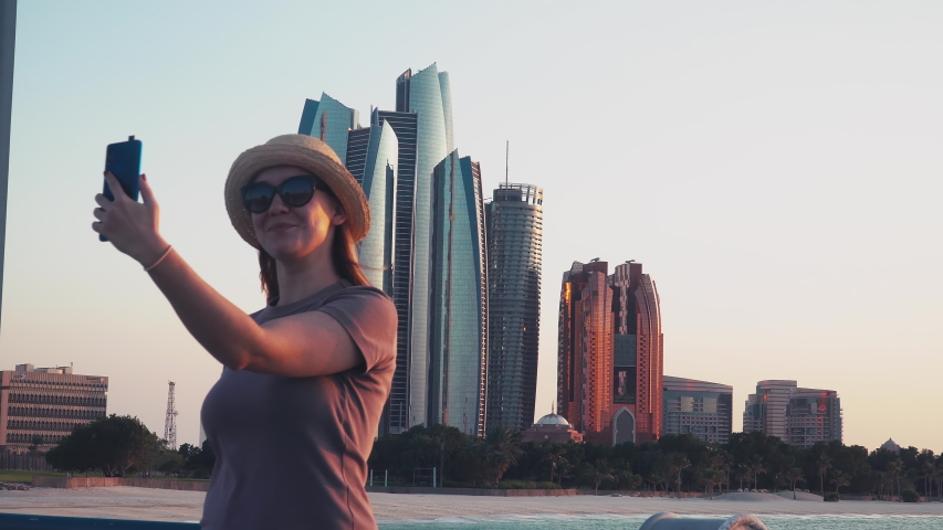 Young Caucasian Female Tourist Taking Selfie Pictures With Abu Dhabi Cityscape With Mobile Phone Woman On Solo Travel Vacation In Arab Middle East Countries