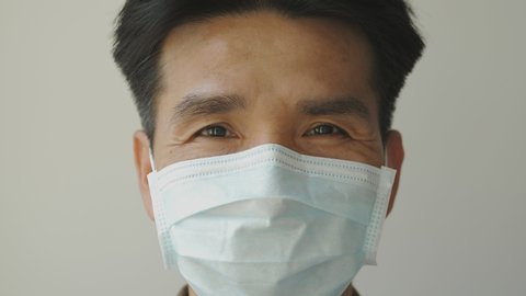 An Asian man wears a face mask to protect against a prevalent disease. He nods with a smiling face under a face mask.