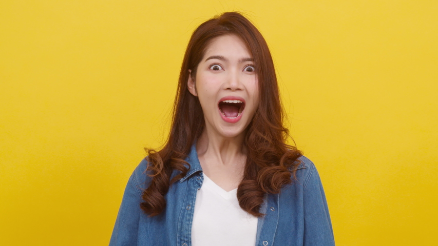 Portrait young Asian lady with positive expression, joyful surprise funky, dressed in casual cloth and looking at camera over yellow background. Happy adorable glad woman rejoices success. Slow motion | Shutterstock HD Video #1047226288