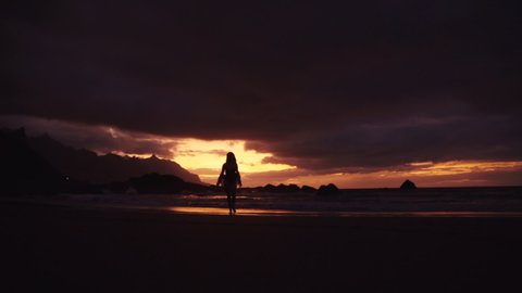 silhouette of a sexy woman walking to the beach from the sea red sunset dramatic sky relax enjoying travel waves rocks stones cloudy romantic evening slow motion