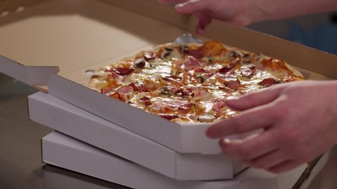 Close up hands professional chef puts just now cooked pizza from oven inside a pizza box ready for delivery recipe take-out meat hot eat take-away box slow motion