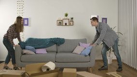 Full length view of smiling couple moving couch and showing thumbs up