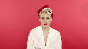Serious blonde pin up woman blinking on pink background