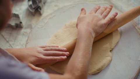 Top view of girl hands rolling dough on table with mother at kitchen. Close up daughter using rolling pin for cookies on domestic kitchen in slow motion. Family cooking together at home.