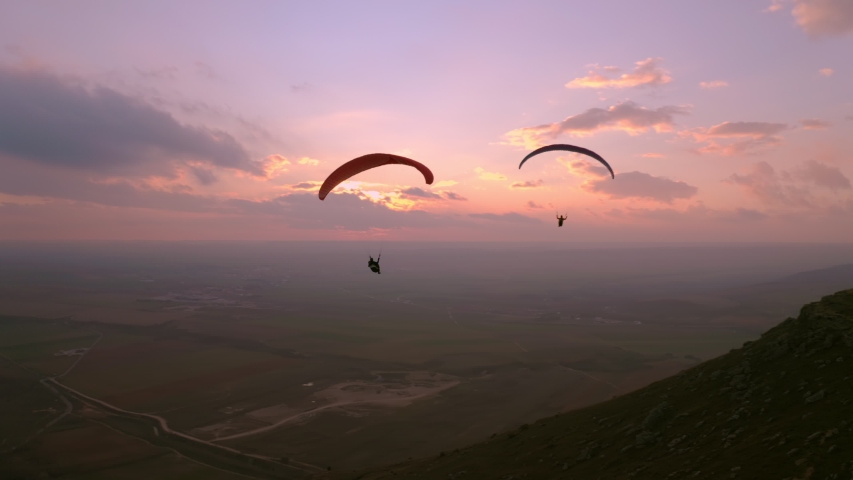 Two paragliders fly over mountain top in epic pink sunset light. Parachutes or paragliding experience. Adrenaline and extreme sport. Beautiful tranquil and calm time in nature Royalty-Free Stock Footage #1047234415