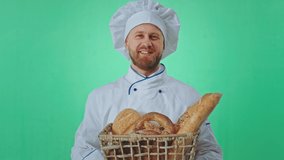 Baker man in the uniform holding in front of the camera basket of a fresh bread he smelling the bread taking video inside of a green studio background
