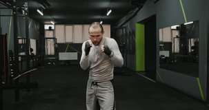 MMA fighter man in grey training suit practicing series of kick punches against camera in gym