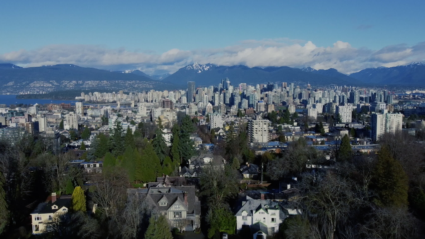 Closing shot of Vancouver downtown with the snow peaks of mountains behind and green trees in front